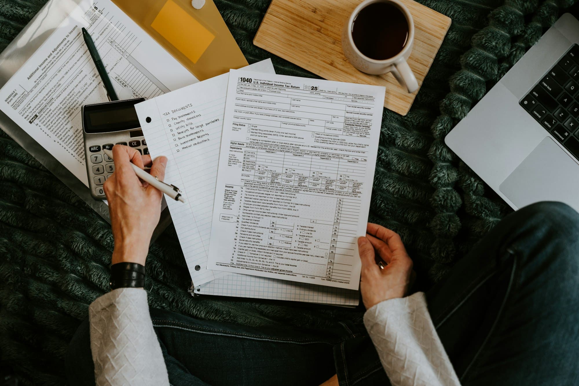 Hands hold a pen over printed forms beside a calculator and a cup of coffee