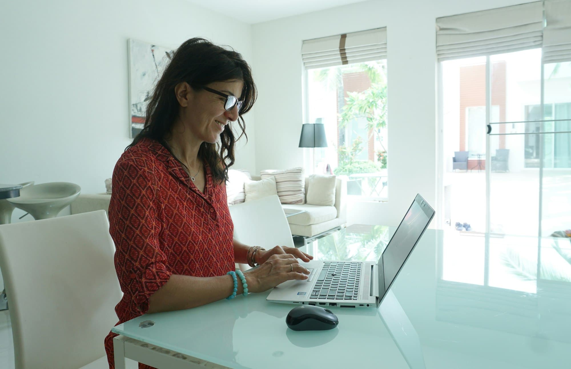 A woman works at a laptop at a table in a bright living room